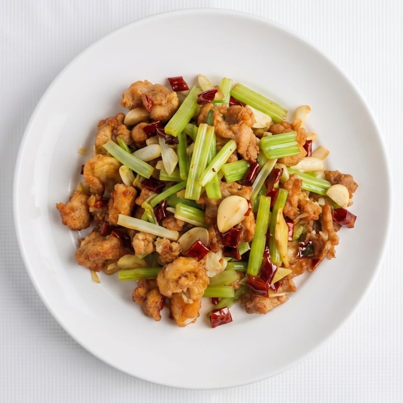 Stir-fried chicken with celery, garlic, and red chili peppers on a white plate.
