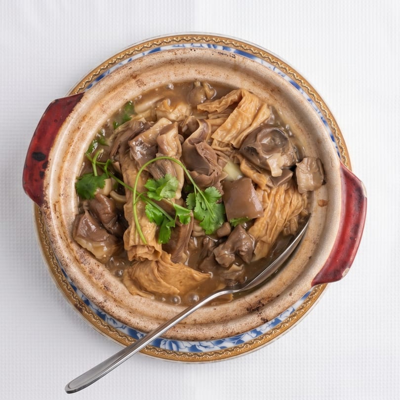 Claypot dish with mushrooms, tofu skin, and cilantro in a savory sauce, served on a white tablecloth.