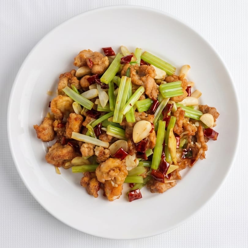 Spicy Kung Pao chicken with celery, peanuts, and chili peppers on a white plate.